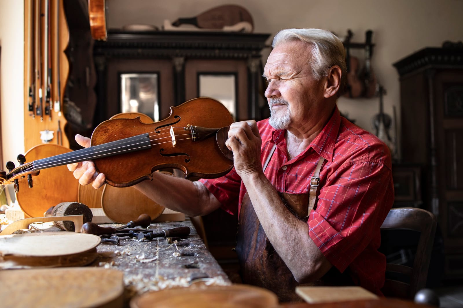 Idoso luthier segurando um violino terminado à luz em sua bancada de trabalho