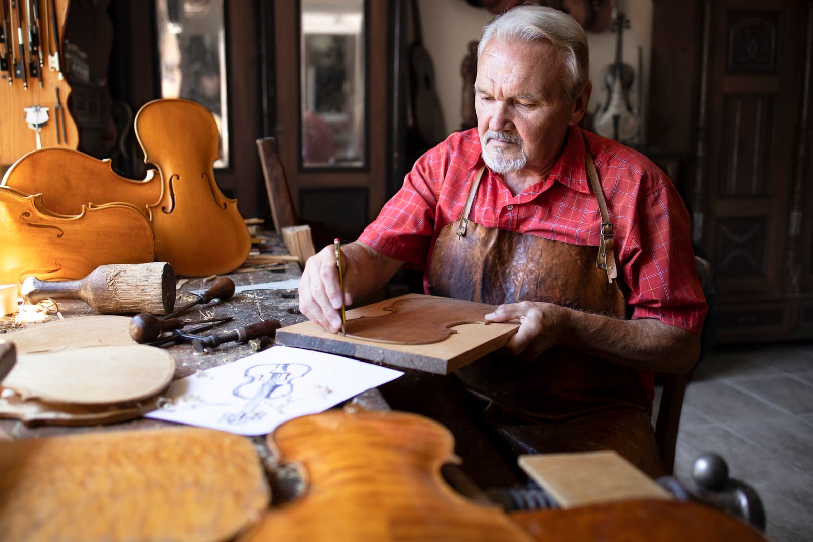 Idoso luthier traçando o molde de um violino em sua oficina de marcenaria